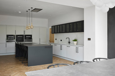 This is an example of a large contemporary open plan kitchen in Other with an integrated sink, quartz worktops, white splashback, marble splashback, black appliances, light hardwood flooring, an island and black worktops.