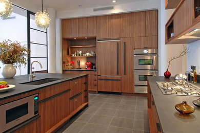Example of a large trendy galley ceramic tile and gray floor eat-in kitchen design in New York with an undermount sink, flat-panel cabinets, brown cabinets, quartz countertops, black backsplash, stone slab backsplash, stainless steel appliances, an island and black countertops