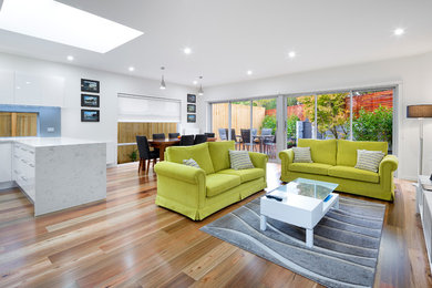 This is an example of a mid-sized modern open concept living room in Melbourne with white walls, light hardwood floors, no fireplace and a freestanding tv.