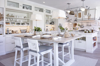 This is an example of a large country l-shaped open plan kitchen in Barcelona with an undermount sink, white cabinets, marble benchtops, white splashback, stone slab splashback, white appliances, light hardwood floors, with island and recessed-panel cabinets.