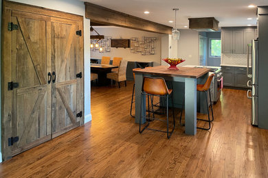 Trendy medium tone wood floor eat-in kitchen photo in Other with recessed-panel cabinets, gray cabinets, wood countertops, white backsplash, ceramic backsplash, stainless steel appliances, an island and brown countertops
