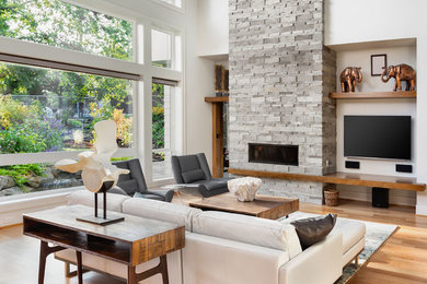 Imagen de salón abierto moderno grande con paredes blancas, suelo de madera en tonos medios, todas las chimeneas, marco de chimenea de piedra y televisor colgado en la pared