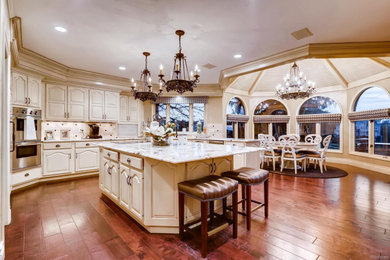 Inspiration for a mid-sized timeless u-shaped dark wood floor and brown floor eat-in kitchen remodel in Denver with an undermount sink, raised-panel cabinets, beige cabinets, granite countertops, multicolored backsplash, stone tile backsplash, paneled appliances, two islands and white countertops