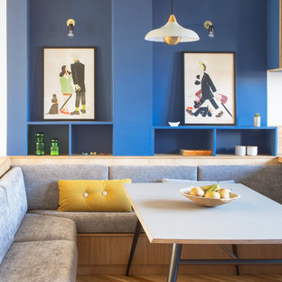 Cette image montre une salle à manger ouverte sur le salon design de taille moyenne avec un mur bleu, un sol en bois clair et un sol beige.