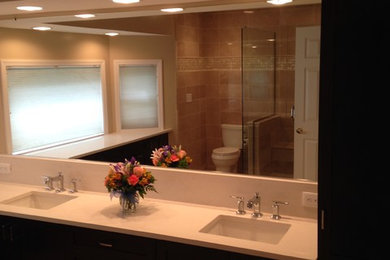 Example of a large transitional master brown tile and stone tile corner shower design in Boston with flat-panel cabinets, dark wood cabinets, a two-piece toilet, brown walls, an undermount sink and solid surface countertops