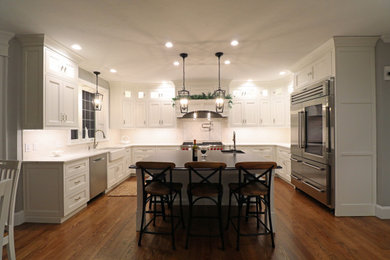 This is an example of a large transitional u-shaped eat-in kitchen in Boston with a farmhouse sink, beaded inset cabinets, white cabinets, quartz benchtops, white splashback, ceramic splashback, stainless steel appliances, medium hardwood floors, with island, multi-coloured floor and white benchtop.