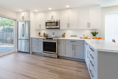 Example of a mid-sized transitional galley vinyl floor eat-in kitchen design in Vancouver with a double-bowl sink, shaker cabinets, gray cabinets, laminate countertops, white backsplash, subway tile backsplash, stainless steel appliances and a peninsula