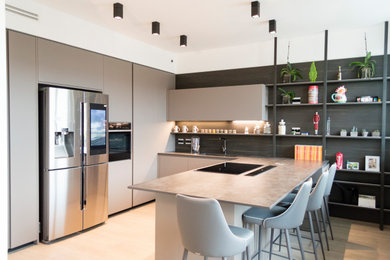 Photo of a large modern u-shaped open plan kitchen in Other with an integrated sink, beaded inset cabinets, black appliances, light hardwood floors and a peninsula.