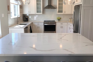 Example of a large transitional u-shaped medium tone wood floor and brown floor open concept kitchen design in Denver with a single-bowl sink, shaker cabinets, white cabinets, quartzite countertops, white backsplash, subway tile backsplash, stainless steel appliances, an island and white countertops