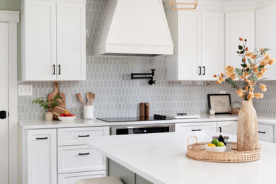This is an example of a mid-sized transitional u-shaped eat-in kitchen in Baltimore with a farmhouse sink, shaker cabinets, white cabinets, quartz benchtops, green splashback, ceramic splashback, stainless steel appliances, medium hardwood floors, with island, brown floor and white benchtop.