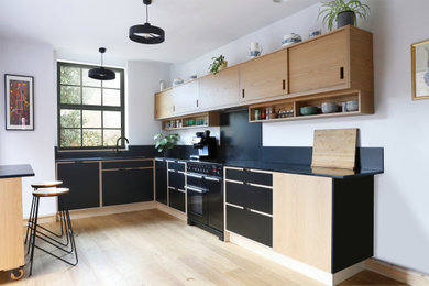 Modelo de cocinas en U escandinavo de tamaño medio con armarios con paneles lisos, puertas de armario de madera clara, encimera de cuarzo compacto y encimeras negras