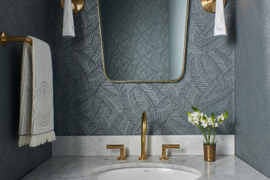 Example of a small trendy wallpaper powder room design in Charlotte with brown cabinets, blue walls, a drop-in sink, gray countertops and a built-in vanity