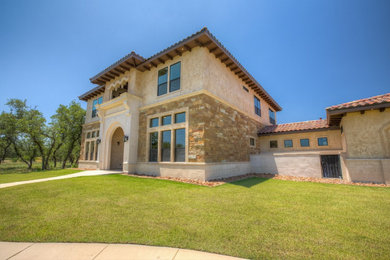 Inspiration for a large mediterranean two-story stone house exterior remodel in Austin with a hip roof, a tile roof and a brown roof