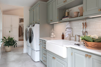 Inspiration for a large timeless ceramic tile and gray floor laundry room remodel in Burlington with a farmhouse sink, raised-panel cabinets, green cabinets, quartz countertops, white backsplash, subway tile backsplash, white walls, a side-by-side washer/dryer and white countertops