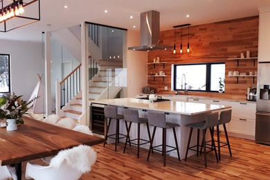 Open concept kitchen - small rustic galley light wood floor open concept kitchen idea in Montreal with a farmhouse sink, shaker cabinets, white cabinets, quartz countertops, wood backsplash, stainless steel appliances and an island