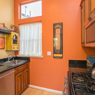 Cette photo montre une petite arrière-cuisine tendance en U avec aucun îlot, un placard avec porte à panneau surélevé, des portes de placard en bois brun, un plan de travail en granite, une crédence orange, un électroménager en acier inoxydable, un évier posé et un sol en bambou.