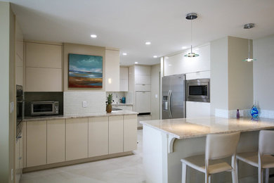 Minimalist kitchen photo in Miami with an undermount sink, flat-panel cabinets, white cabinets, granite countertops, white backsplash, mosaic tile backsplash, stainless steel appliances and a peninsula