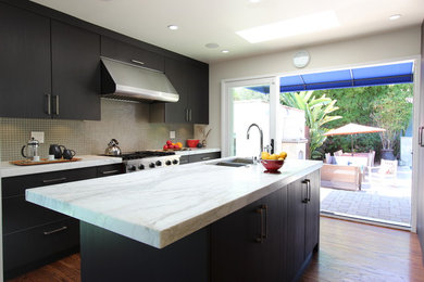 Photo of a mid-sized transitional galley eat-in kitchen in Los Angeles with an undermount sink, flat-panel cabinets, dark wood cabinets, marble benchtops, grey splashback, glass tile splashback, stainless steel appliances, medium hardwood floors and with island.