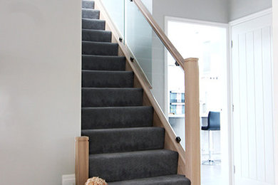 Photo of a medium sized modern carpeted straight glass railing staircase in West Midlands with carpeted risers.