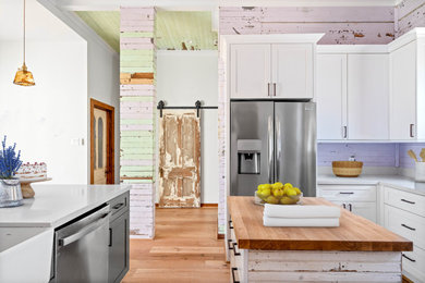 Eat-in kitchen - mid-sized cottage u-shaped light wood floor eat-in kitchen idea in Houston with a farmhouse sink, shaker cabinets, white cabinets, quartzite countertops, stainless steel appliances, an island and gray countertops