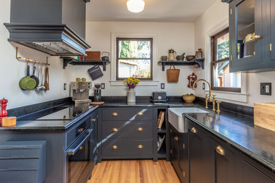 Kitchen pantry - small craftsman u-shaped medium tone wood floor and brown floor kitchen pantry idea in San Francisco with a farmhouse sink, glass-front cabinets, blue cabinets, soapstone countertops, gray backsplash, stone slab backsplash, paneled appliances, no island and black countertops