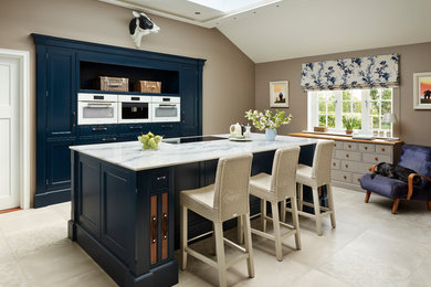 Design ideas for a mid-sized traditional kitchen in Essex with beaded inset cabinets, blue cabinets, marble benchtops, white appliances, with island and grey floor.