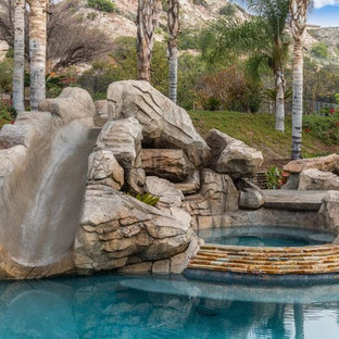Exotisk inredning av en stor anpassad pool på baksidan av huset, med vattenrutschkana och marksten i betong