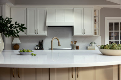 Large transitional single-wall medium tone wood floor, brown floor and vaulted ceiling eat-in kitchen photo in Philadelphia with a farmhouse sink, recessed-panel cabinets, beige cabinets, quartz countertops, white backsplash, quartz backsplash, stainless steel appliances, an island and white countertops
