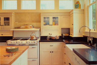 Inspiration for a mid-sized craftsman u-shaped medium tone wood floor and beige floor eat-in kitchen remodel in San Francisco with a farmhouse sink, shaker cabinets, beige cabinets, granite countertops, black backsplash, granite backsplash, white appliances, an island and black countertops