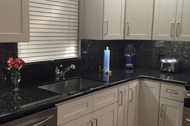 Example of a mid-sized transitional kitchen design in Miami with a single-bowl sink, shaker cabinets, white cabinets, granite countertops, black backsplash, stone slab backsplash and stainless steel appliances