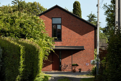 Imagen de fachada de casa roja y negra tradicional de tamaño medio de dos plantas con revestimiento de ladrillo, tejado a dos aguas y tejado de metal