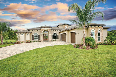 Photo of a large contemporary one-storey stucco beige house exterior in Orlando with a clipped gable roof and a shingle roof.