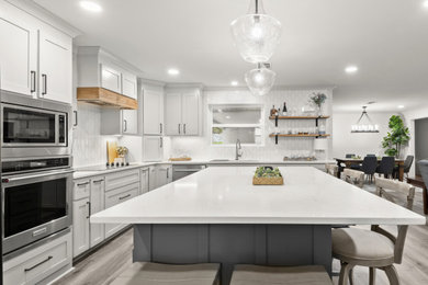 Eat-in kitchen - mid-sized transitional l-shaped vinyl floor and gray floor eat-in kitchen idea in New Orleans with an undermount sink, shaker cabinets, gray cabinets, quartz countertops, white backsplash, porcelain backsplash, stainless steel appliances, an island and white countertops