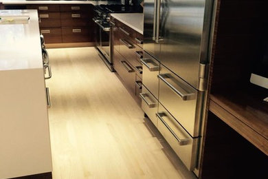 Example of a large l-shaped light wood floor open concept kitchen design in New York with an integrated sink, flat-panel cabinets, white cabinets, blue backsplash, glass sheet backsplash, stainless steel appliances and an island