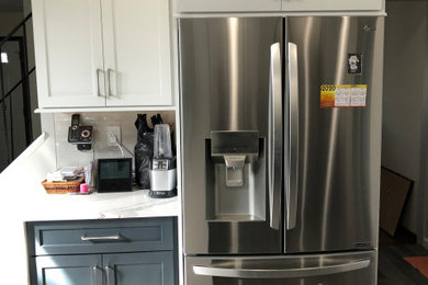 Mid-sized transitional l-shaped porcelain tile and gray floor enclosed kitchen photo in New York with an undermount sink, shaker cabinets, white cabinets, quartz countertops, white backsplash, porcelain backsplash, stainless steel appliances, a peninsula and white countertops