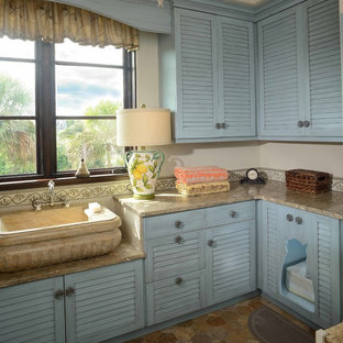 Diseño de lavadero en L, costero, de tamaño medio, con puertas de armario azules, armarios con puertas mallorquinas, paredes beige, fregadero de un seno, encimera de piedra caliza, suelo de piedra caliza y encimeras beige