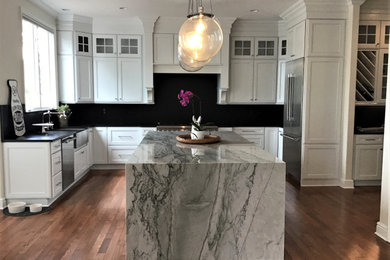 Eat-in kitchen - large transitional u-shaped medium tone wood floor and brown floor eat-in kitchen idea in Other with a farmhouse sink, flat-panel cabinets, white cabinets, quartzite countertops, black backsplash, stone slab backsplash, stainless steel appliances, an island and black countertops