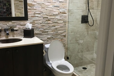 Photo of a mid-sized mediterranean 3/4 bathroom in Miami with dark wood cabinets, an alcove shower, a one-piece toilet, brown tile, stone tile, brown walls, travertine floors, an undermount sink, engineered quartz benchtops, brown floor, a hinged shower door and white benchtops.