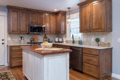 Mid-sized elegant l-shaped medium tone wood floor and brown floor enclosed kitchen photo in Grand Rapids with an undermount sink, raised-panel cabinets, dark wood cabinets, quartz countertops, beige backsplash, stone tile backsplash, stainless steel appliances, an island and beige countertops