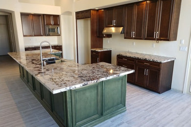 Example of a mid-sized tuscan l-shaped porcelain tile and gray floor eat-in kitchen design in Phoenix with an undermount sink, raised-panel cabinets, green cabinets, granite countertops, stainless steel appliances, an island and white countertops