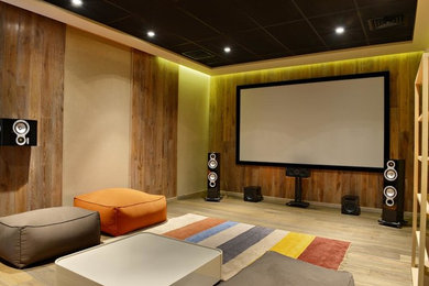Photo of a large contemporary enclosed home theatre in Denver with multi-coloured walls, light hardwood floors, a projector screen and brown floor.
