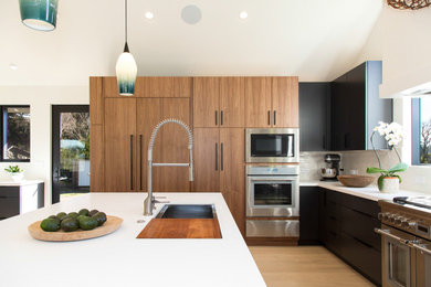 Large 1960s u-shaped light wood floor, brown floor and vaulted ceiling open concept kitchen photo in San Francisco with an undermount sink, flat-panel cabinets, black cabinets, quartz countertops, white backsplash, ceramic backsplash, paneled appliances, an island and white countertops