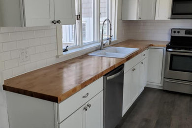 Inspiration for a farmhouse l-shaped vinyl floor and brown floor eat-in kitchen remodel in Other with a farmhouse sink, shaker cabinets, white cabinets, wood countertops, white backsplash, ceramic backsplash and stainless steel appliances