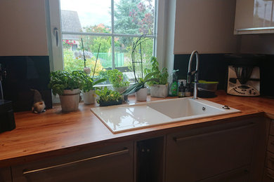 Offene, Große Moderne Küche ohne Insel in U-Form mit Einbauwaschbecken, flächenbündigen Schrankfronten, grauen Schränken, Mineralwerkstoff-Arbeitsplatte, Küchenrückwand in Schwarz, Glasrückwand, schwarzen Elektrogeräten, braunem Holzboden, braunem Boden und brauner Arbeitsplatte in Berlin