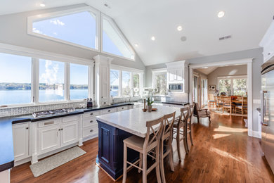 Eat-in kitchen - large contemporary u-shaped medium tone wood floor, brown floor and vaulted ceiling eat-in kitchen idea in Charlotte with a farmhouse sink, recessed-panel cabinets, white cabinets, quartzite countertops, white backsplash, marble backsplash, stainless steel appliances, an island and black countertops