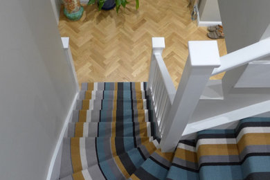 Photo of a mid-sized contemporary carpeted l-shaped staircase in Wiltshire with carpet risers, wood railing and wallpaper.