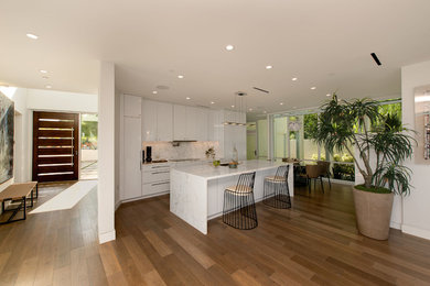Open concept kitchen - mid-sized modern galley medium tone wood floor and brown floor open concept kitchen idea in Los Angeles with a single-bowl sink, flat-panel cabinets, white cabinets, marble countertops, white backsplash, marble backsplash, paneled appliances, an island and white countertops
