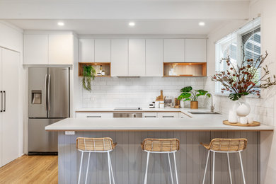 This is an example of a mid-sized contemporary u-shaped eat-in kitchen in Adelaide with a single-bowl sink, white cabinets, laminate benchtops, white splashback, subway tile splashback, stainless steel appliances, medium hardwood floors, a peninsula, brown floor and white benchtop.