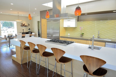 Photo of a large midcentury galley eat-in kitchen in San Francisco with stainless steel appliances, yellow splashback, glass tile splashback, light wood cabinets, flat-panel cabinets, an undermount sink, quartz benchtops, dark hardwood floors, with island and brown floor.