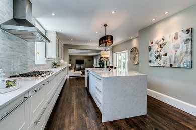 Example of a trendy dark wood floor and brown floor kitchen design in Wilmington with an undermount sink, flat-panel cabinets, white cabinets, quartzite countertops, white backsplash, marble backsplash, stainless steel appliances, an island and white countertops